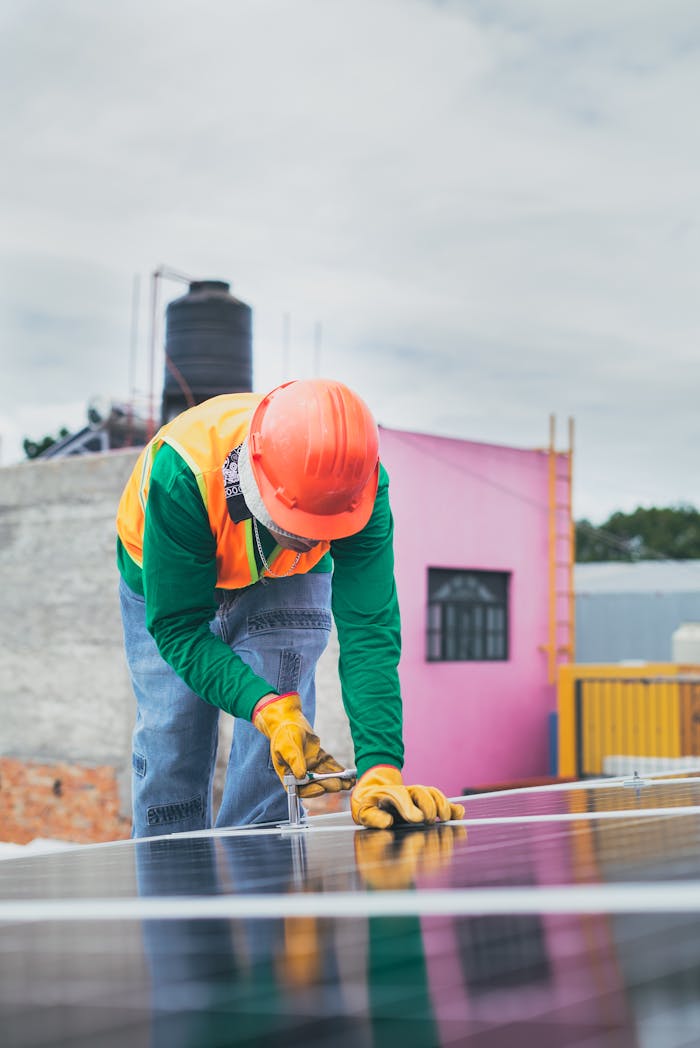 A solar technician working outdoors installing photovoltaic panels with safety gear.